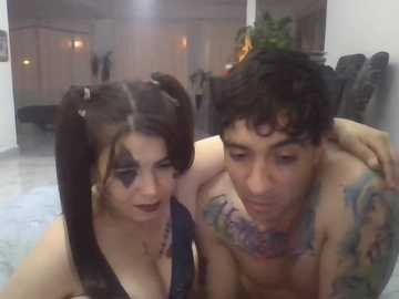 Video of a tattooed man and woman in a dimly lit living room, both with goth makeup, including black eyeliner and dark lipstick.