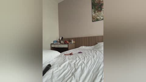 Video of a dimly lit, simple bedroom with a white bed, a wooden nightstand holding a lamp and a framed floral painting, and a white pillow with a red lipstick mark.