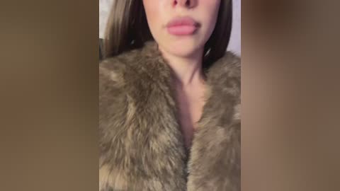 Video of a woman's face and shoulders, wearing a brown, faux-fur coat. Her lips are slightly parted, revealing a hint of lipstick. Background is blurred, focusing attention on the coat's texture and her smooth skin.