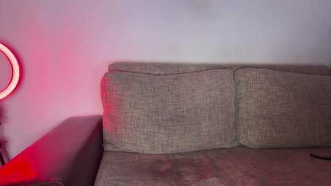 Video of a beige couch with a circular red light on the left, against a white wall, creating a warm, dim ambiance.