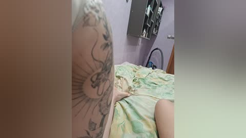 Video of a tattooed arm on a bed with a pastel floral duvet, purple walls, and a silver-framed mirror, capturing a casual, intimate bedroom scene.