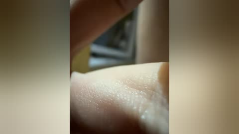 A close-up video of a human finger gently touching a smooth, light-colored skin surface, likely a breast. The background is blurred, featuring an indistinct yellow and green color palette.