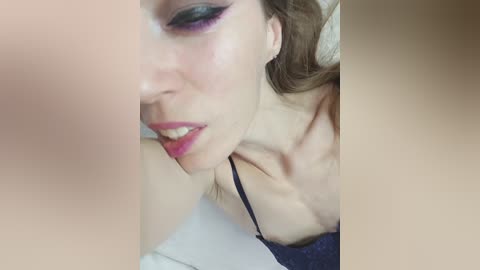 Video of a fair-skinned woman with light brown hair, wearing purple eyeshadow, smiling, with a blurred person's hand partially obscuring the frame.