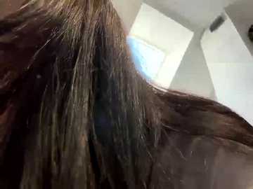 A close-up video of a woman's long, dark brown hair with slight waves, viewed from behind. The background features a modern, minimalist interior with white walls and a window.
