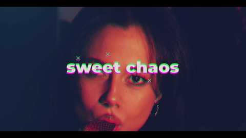 Video of a woman with dark hair and fair skin, close-up of her face, blurred background, text overlay \"sweet chaos\" in colorful, glitchy font.