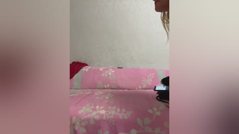 A video of a woman with wet hair lying on a pink bed with a floral design, holding a phone, in a dimly lit room.