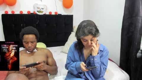 A video shows a naked man with a beard and a woman in a blue shirt, both focused on a tablet. Background includes balloons and a bed, with text overlaying the image.