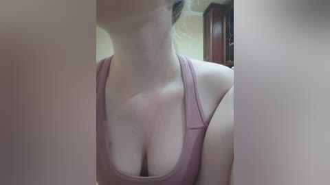 Video of a light-skinned woman with auburn hair, wearing a pink tank top that reveals cleavage. The image is slightly blurred, focusing on her upper body and neck.