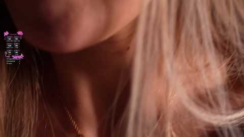 A close-up video of a woman's neck and shoulder, featuring fair skin, long blonde hair, and a delicate gold necklace. The background is blurred, with digital overlays showing a chat interface and a video call screen.