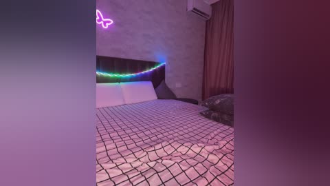 A video of a modern bedroom with a bed adorned with a black-and-white geometric-patterned duvet, a neon butterfly light, and an air conditioner on the wall. The room features a minimalist, chic design.