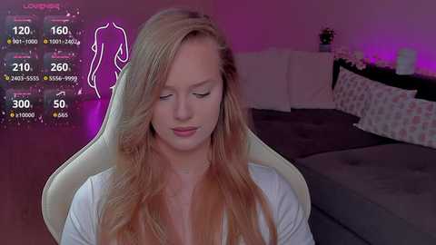 Video of a blonde, fair-skinned woman with long hair, sitting on a beige gaming chair, in a dimly lit room with purple ambient lighting.