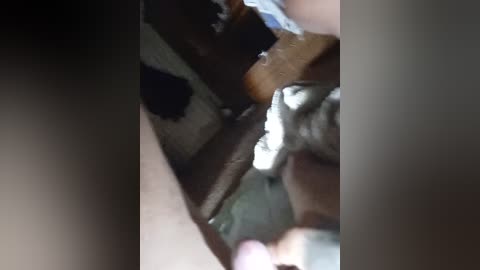 A close-up video of a person's hand working on a wooden object, possibly a piece of furniture or a small wooden structure. The image is slightly blurred, with a focus on the hand and the woodwork.