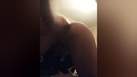 Video of a naked, light-skinned person with a slender build, bent over, in a dimly lit room with a wooden door. The image is grainy, low-resolution, and blurry, making it difficult to discern details clearly.