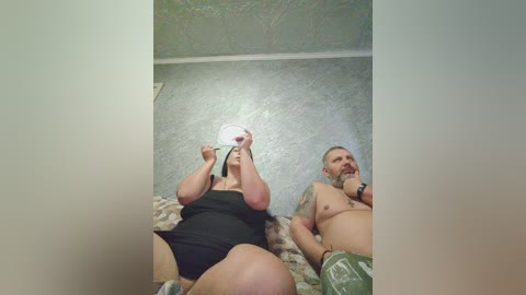 Video of a middle-aged, overweight woman and man on a bed with a textured green ceiling, both topless, the man with a beard.