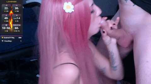 A video shows a pink-haired woman with a daisy headband performing oral sex on a naked man, while a digital screen displays a \"Loving\" notification.