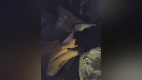 Video of a person lying on a bed with dark, possibly black, hair and a yellow shirt, under dim lighting. The background features pillows and a blurred, dark environment.