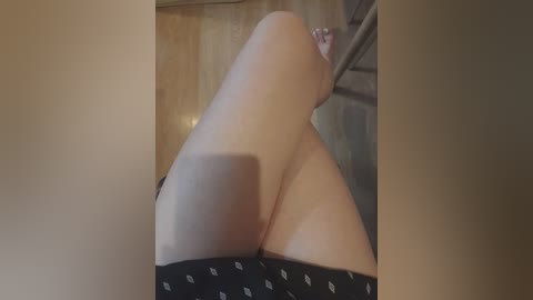 A video of a woman's lower body in black panties, lying on a wooden floor, with a blurred background of a wooden door and wall.