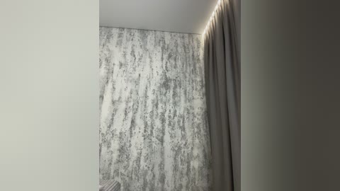 A video of a modern room with a textured gray wall and beige curtain. The room's ceiling is white, creating a minimalist, serene atmosphere.