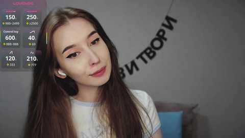 Video of a young Asian woman with long brown hair, wearing a white shirt, smiling softly. Background includes a weather app and a black banner with Russian text.