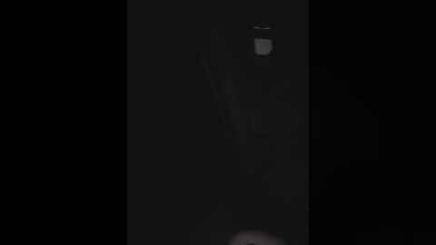 A dimly lit video features a person in a dark, narrow hallway, likely a teenager, partially obscured by shadows, wearing a hoodie and jeans, with a small light source visible at the top right.