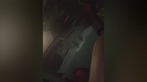 A dimly lit video of a person's face, with a reflection of a shiny object on their glasses. The background is dark and indistinct, with a slight glow from an unseen source.