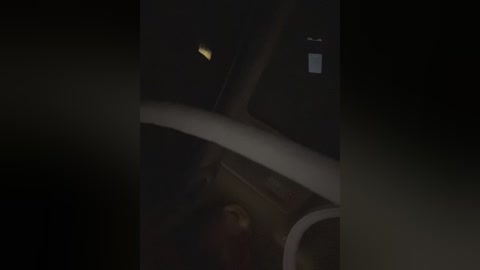 A dimly lit, nighttime video of a car interior, showing the steering wheel, dashboard, and a faint, glowing yellow light source, possibly from a phone or a GPS device. The image is dark and slightly blurry.