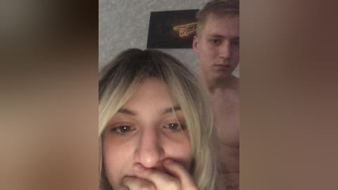 Video of a blonde woman with a light complexion and a man with short blonde hair, both naked in a dimly lit room with wallpaper.