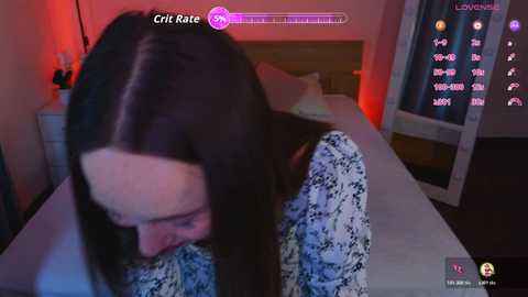 A video of a woman with long black hair, wearing a floral-patterned dress, lying on a bed with a wooden headboard, surrounded by dim red lighting and a video game screen with a 'Crate Rate' display.