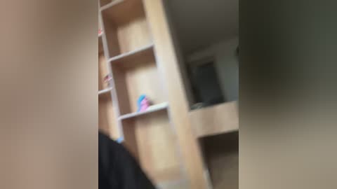 A blurry video of a wooden loft bed with multiple shelves, featuring colorful toys and books, set against a beige wall in a dimly lit room.