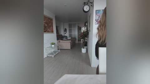 A video of a modern living room with light wood flooring, white walls, a pink sofa, and a round clock on a white wall.