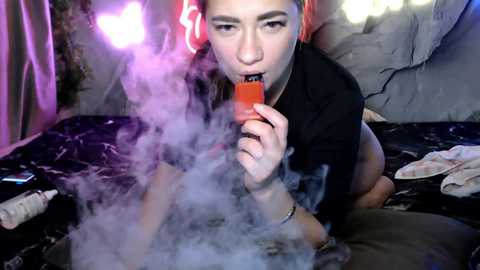 A young woman with light skin and dyed red hair, wearing a black top, is smoking a small orange vape pen, surrounded by purple and pink neon lights and a messy room.