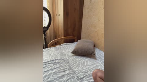A video of a rustic, sparsely furnished bedroom with a wooden bed, beige walls, a small window, and a vintage fan. The room has a simple, minimalistic design.