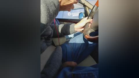 Video of a man in a gray sweater assisting another man in a blue shirt into a car. The car's interior is visible with a dashboard display showing a blue logo.