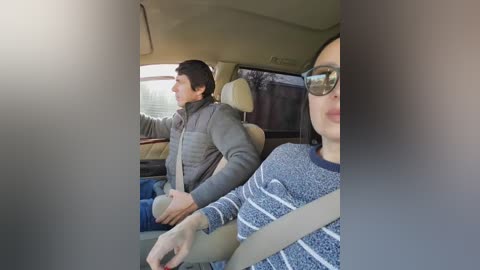 Video of an Asian woman with glasses and a grey sweater, seated in a car's front passenger seat. She is smiling. Behind her, a man in a grey jacket and beige car seat is visible.