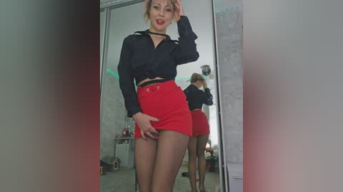 Video of a confident woman with light skin, wearing a black blouse, red mini-skirt, and black tights, posing in front of a mirror, reflecting her figure, in a modern, minimalist room.