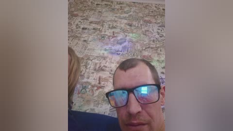 Video of a man with short brown hair and black-framed glasses, wearing a blue shirt, against a colorful, abstract, comic-style wall background.