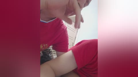 A video captures a man in a red T-shirt, with a blurred background featuring a blue wall and a partially visible door. The image is slightly blurred, giving it a soft focus.