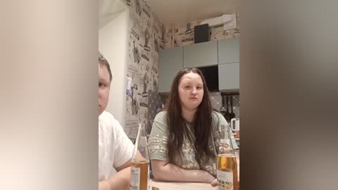 A video shows a young woman with long brown hair, wearing a patterned green shirt, seated at a table in a cluttered room with newspaper-covered walls and a cluttered background.