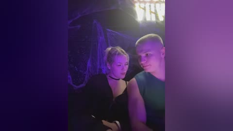 A dimly-lit video of a bald man and a woman with blonde hair, both dressed in black, standing close, illuminated by a purple light, under an umbrella.