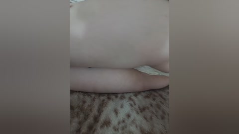 Video of a person's bare buttocks and upper thighs, lying on a brown and beige patterned blanket. The skin is light and smooth. The background is blurred, focusing on the lower body.