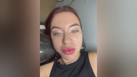 Video of a fair-skinned woman with red hair, wearing a black top, lying on a gray couch with a black cushion. She has pink lipstick and subtle makeup.
