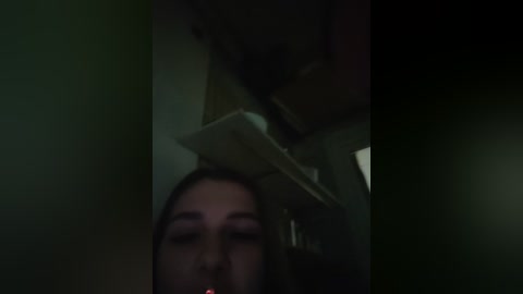 Video of a woman lying on a table, head tilted back, eyes closed, and mouth slightly open, with a dim, greenish lighting creating a moody, intimate atmosphere.