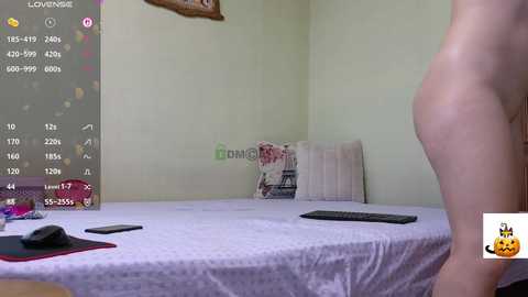 A video of a nude person standing beside a bed with a grey sheet. A digital overlay shows a video game interface and a Twitch logo.