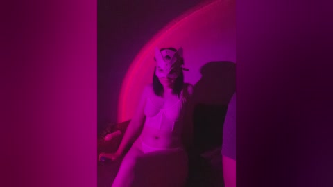 A video of a nude woman with medium breasts, long dark hair, and fair skin, reclining in a chair under intense pink and purple lighting.