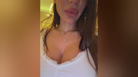 Video of a Caucasian woman with long brown hair, wearing a white tank top with lace trim, sticking out her tongue, indoors with warm lighting.