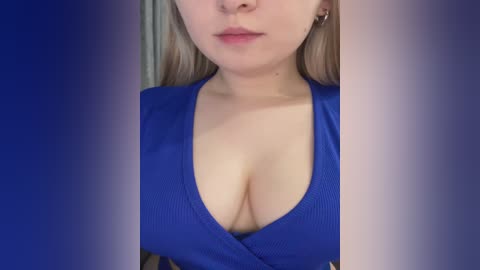 Video of a light-skinned woman with long blonde hair, wearing a deep V-neck blue dress that reveals ample cleavage. The background is a gradient of blue and purple hues.