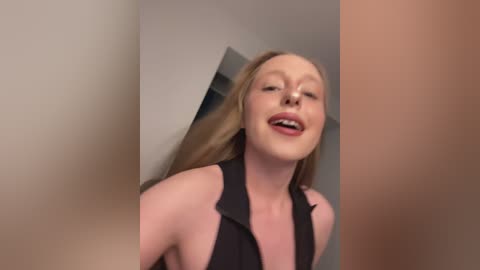 Video of a smiling, fair-skinned woman with long blonde hair, wearing a black halter top, captured from a slightly blurred, angled perspective.
