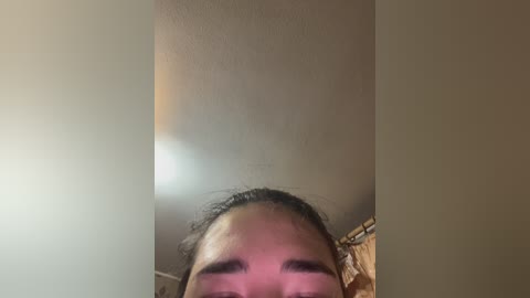 A close-up video of a young person's face, focusing on the eyes and nose, with a slightly blurred background featuring a beige wall and a window.