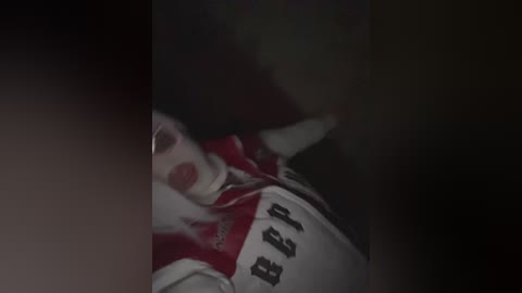 A dimly lit video captures a person in a red and white jacket with \"NBA\" partially visible, lying on a dark surface, possibly injured or unconscious. The image is grainy, with shadows obscuring details.