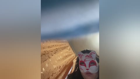 A video featuring a person in a white mask with red markings, wearing a brown, floral-patterned shirt, standing in a dimly lit room with blurred, cloudy sky background.